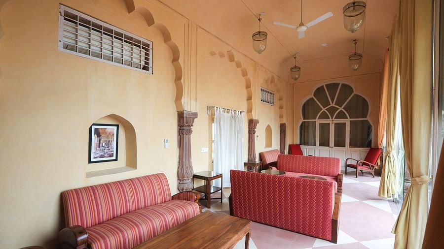 A spacious room features striped sofas, chairs, tables, arched windows, and decorative wall elements at Tijara Fort-Palace - 19th Century, Alwar.