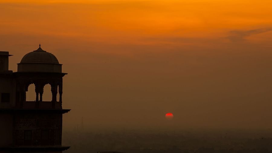 A silhouette of Tijara Fort-Palace's architecture is seen against a vibrant orange sunset sky in Alwar.
