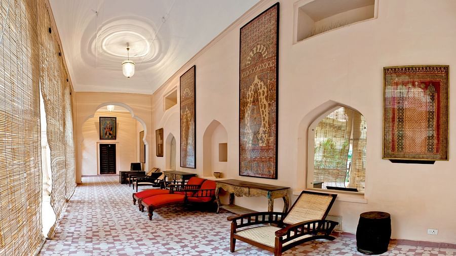 An interior of Neemrana's Tijara Fort Palace in Alwar features tiled flooring, seating, wall art, and arched windows.