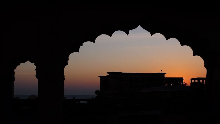 A silhouette of Tijara Fort-Palace's architecture is framed by arched openings against a twilight sky in Alwar.