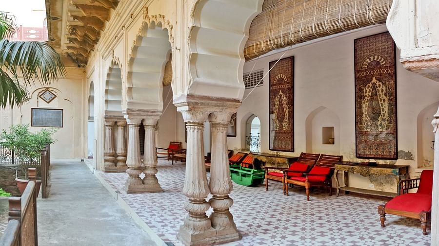 An interior view of Neemrana's Tijara Fort Palace in Alwar shows arched pillars, tiled flooring, seating areas, and decorative wall hangings.