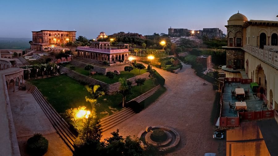 Tijara Fort-Palace in Alwar is beautifully illuminated at dusk, showcasing its architecture and gardens under a twilight sky.