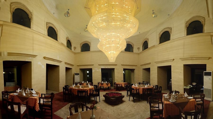 A dining hall with set tables and chairs is illuminated by a large ornate chandelier at Tijara Fort-Palace - 19th Century, Alwar.