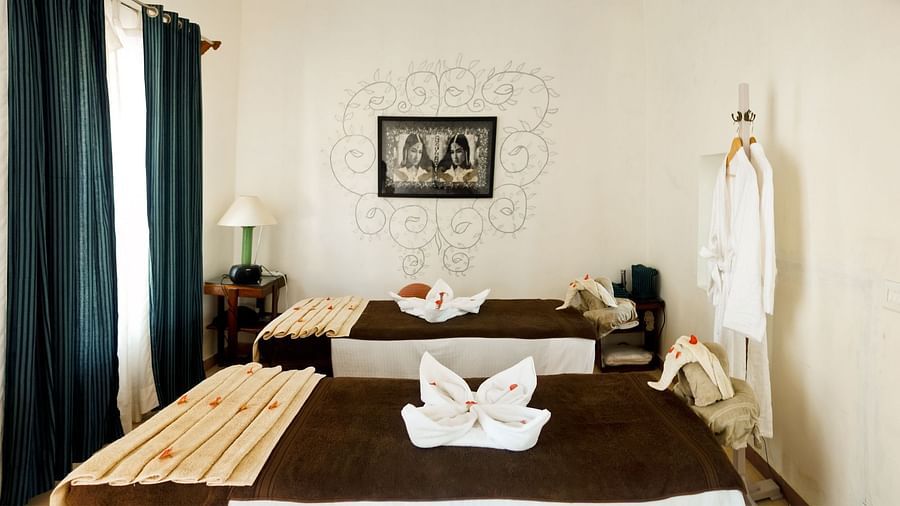 A spa room contains two massage beds with folded towels, robes hanging, and dim lighting at Tijara Fort-Palace - 19th Century, Alwar.