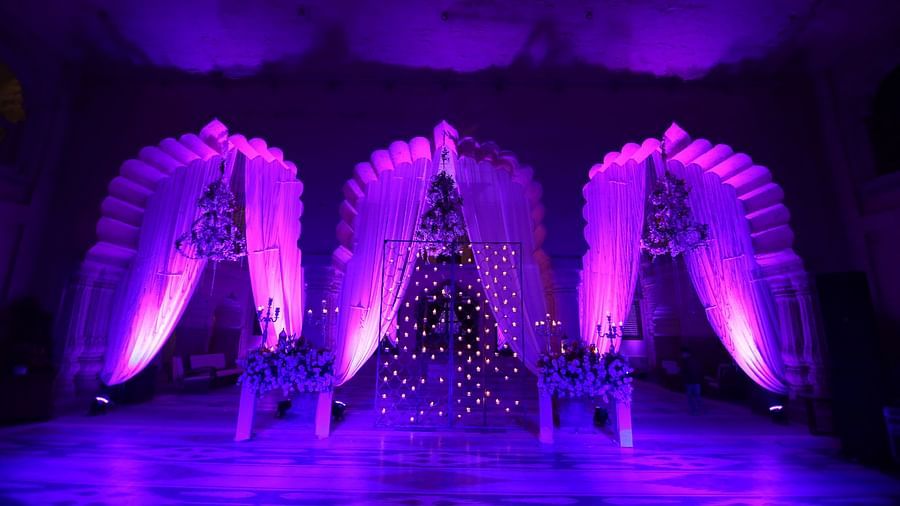 An event stage with ornate backdrops and purple lighting features floral arrangements on pedestals at Tijara Fort-Palace - 19th Century, Alwar.