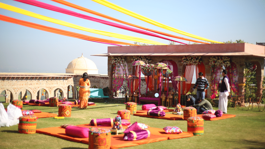 A vibrant outdoor event is set up on a green lawn at Tijara Fort-Palace - 19th Century, Alwar with clear blue sky in the background.