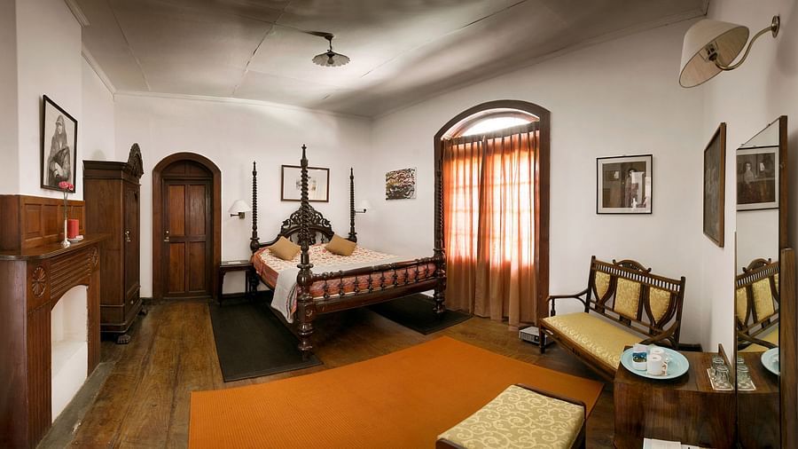 A double bed, a wardrobe, small sofa and a mirror with a chair in front inside Acacia Room- Wallwood Garden - 19th Century, Coonoor