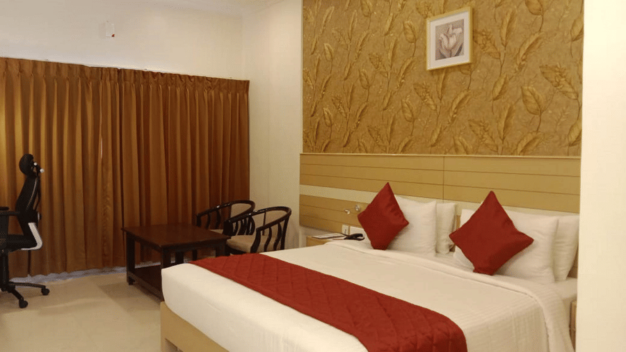 An Executive Room at DSF Grand Plaza, Tuticorin with a king bed in white and red linens against a leaf-patterned feature wall, plus a small seating area by the window.