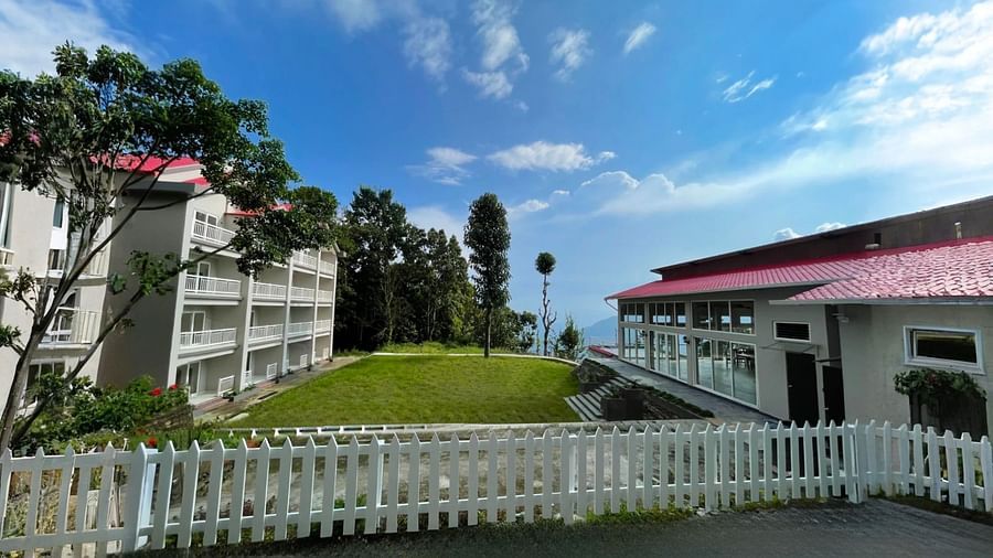 A wide shot of the buildings at Yashshree Resorts & Spa, Kalimpong, with a white fence in the foreground and the beautiful, lush green mountains in the background.