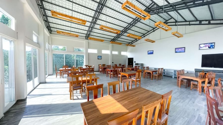 The Dorjeeling Kitchen at the Yashshree Resorts and Spa in Kalimpong featuring a spacious, sunlit dining area with wooden tables and chairs.
