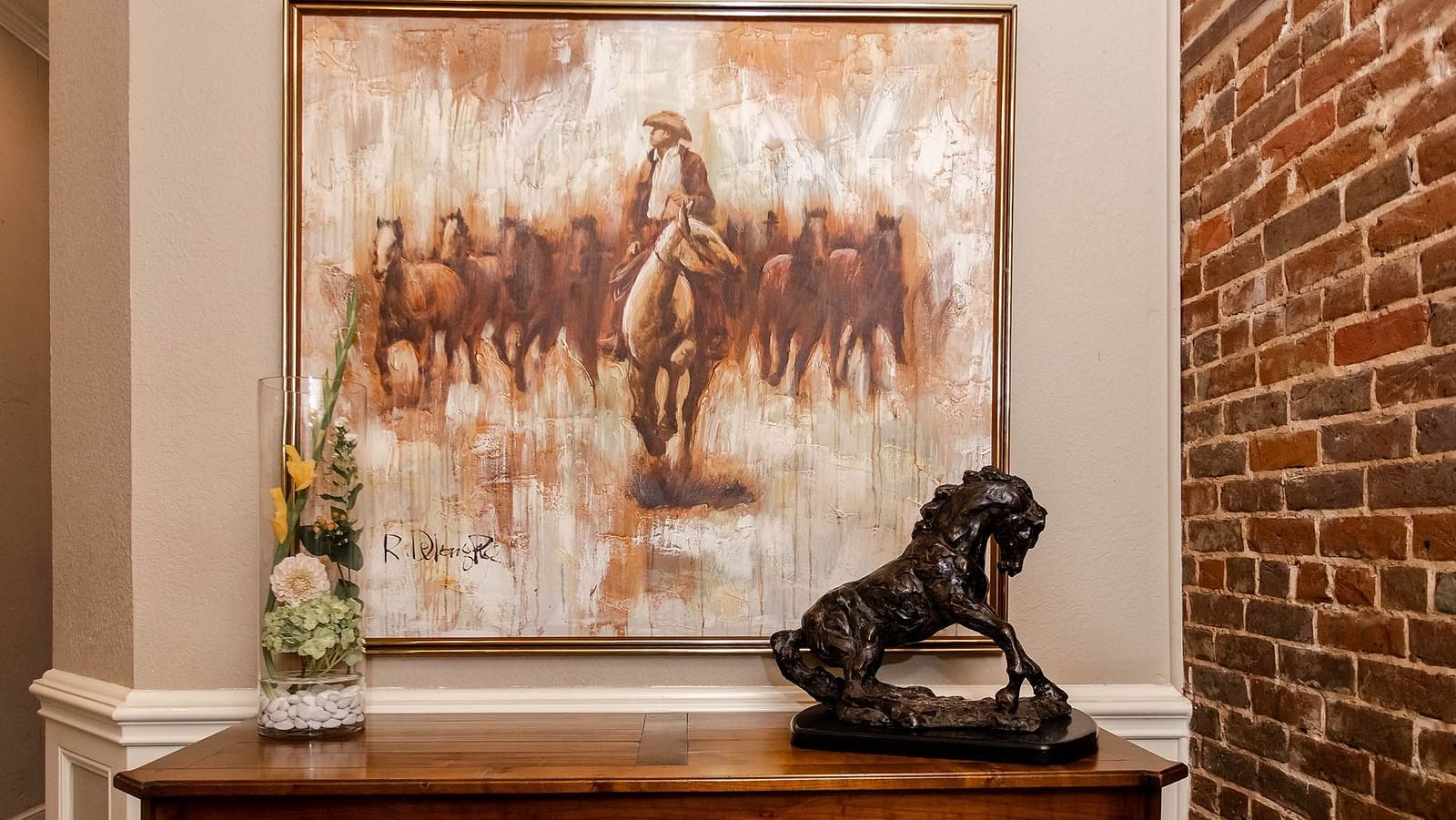 A painting above a wooden cabinet with a decorative sculpture and a small flower vase beside it.- The Grand Hotel & Ballroom, McKinney