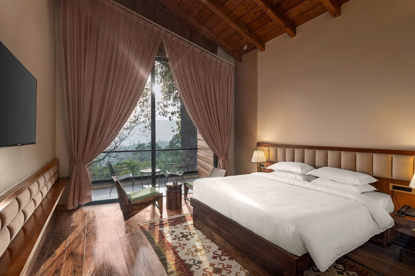 A cosy bedroom with a wooden floor and ceiling, large draped window with a scenic view, and a comfortable sitting area - The Samai, Bhimtal