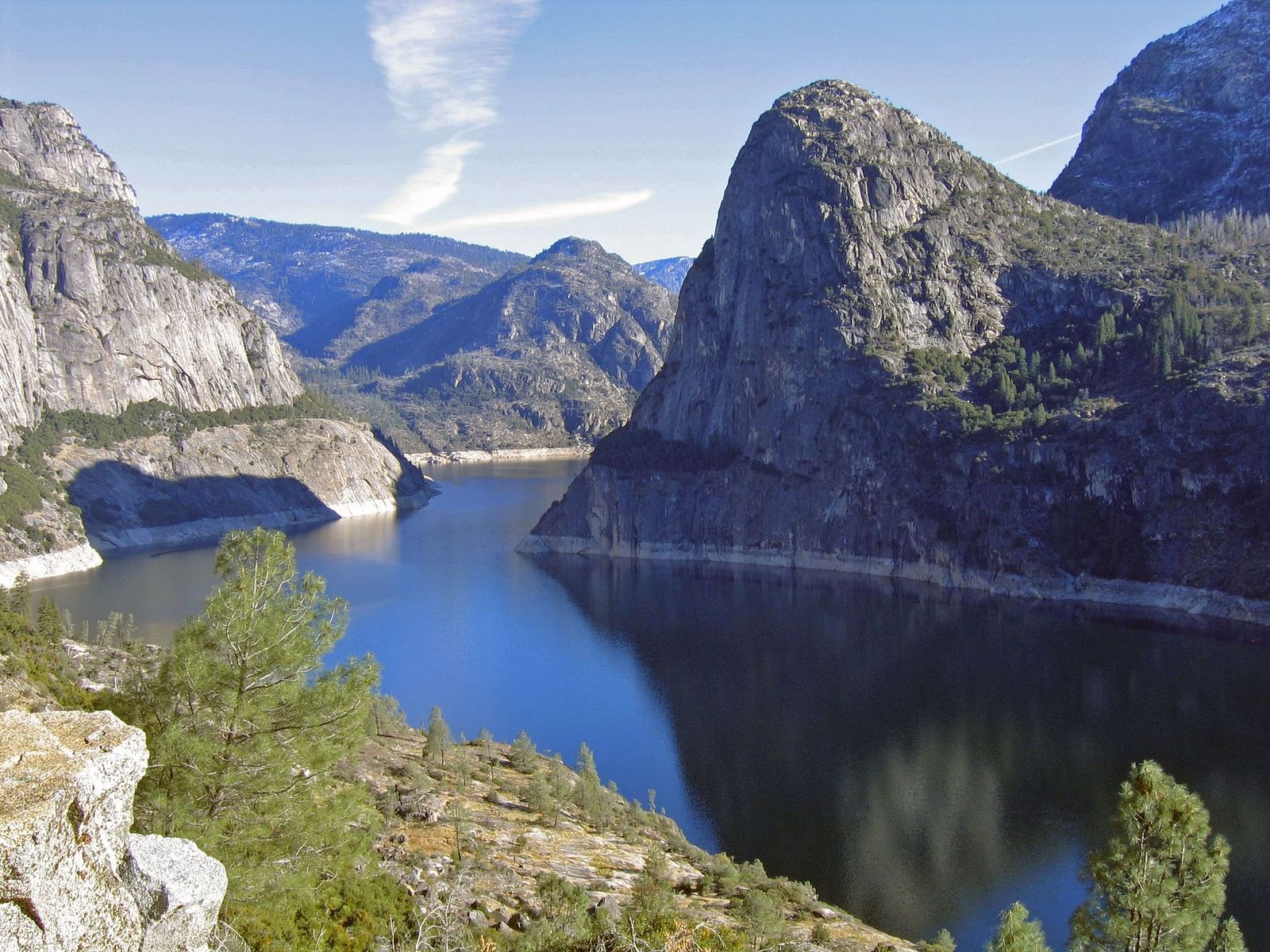 View of the Hetch Hetchy Reservoir, showcasing water flowing between majestic natural mountains under a bright, sunny sky