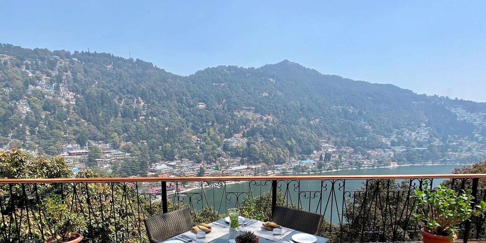 Image showing few chairs placed on the  sides of a square table, pot on either side of the frame, beautifully framed by the backdrop of the mountain ranges.