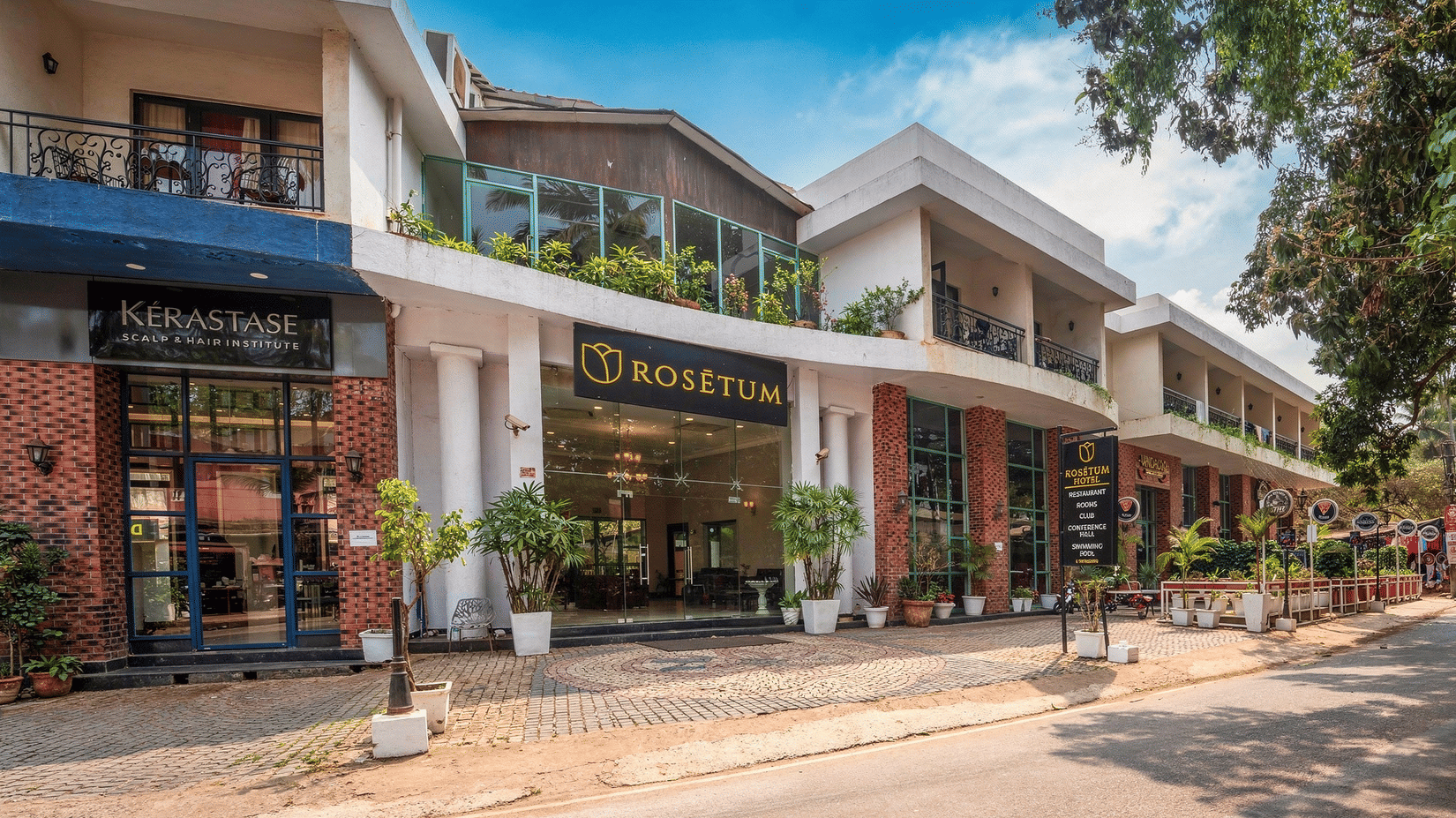 Street-facing exterior of Rosetum Hotels Anjuna with elegant entrance, balcony greenery, and adjacent Kérastase salon