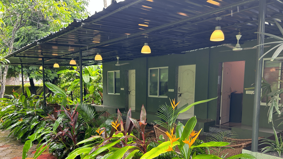 A single-story green building with a covered walkway, hanging lamps, and potted plants at Oceanature Resort, Alibaug.