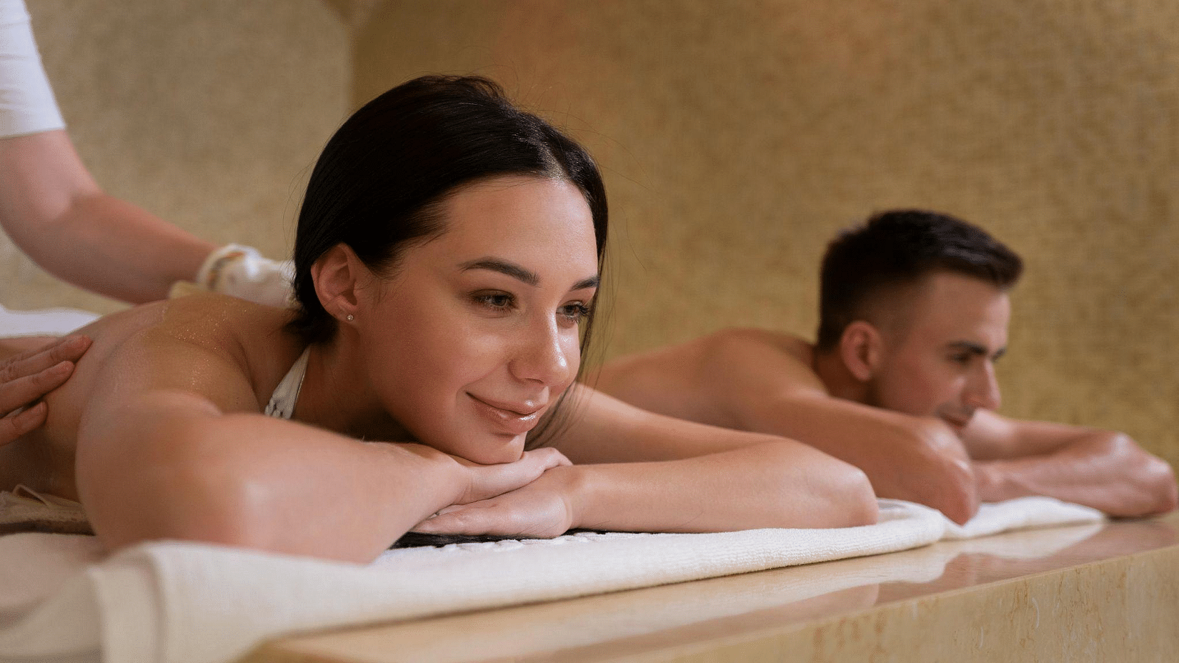 A smiling woman receives a back massage while lying beside a man also getting a massage in a spa setting