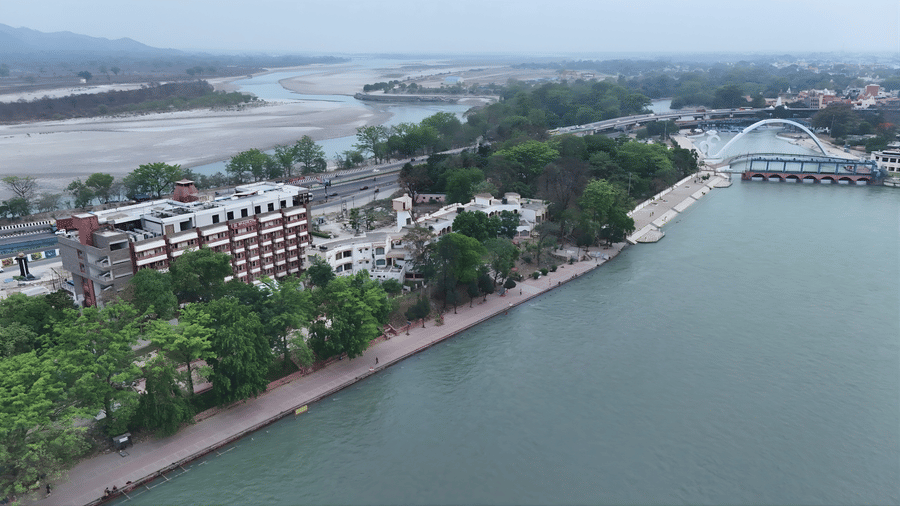 High aerial view of a multi-story hotel situated along a tree-lined waterfront promenade next to a wide river Ganga.