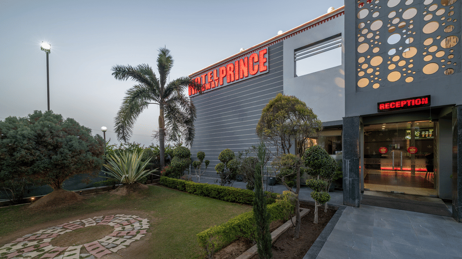 Hotel Highway Prince Paota entrance exterior at dusk with illuminated signage, decorative perforated wall, manicured garden, and warm ambient lighting.