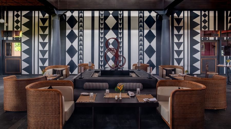 Contemporary lounge-style restaurant seating with woven rattan chairs and bold tribal-patterned wall décor at Baan Kahi, Rhino and River BluSalzz Collection, Pobitora.