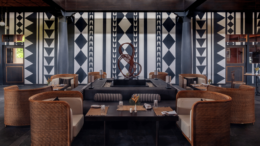 A wide view of the dining hall at Rhino & River Wildlife Retreat & Spa, Pobitora, featuring semi-circular wicker booths and a striking geometric-patterned feature wall.