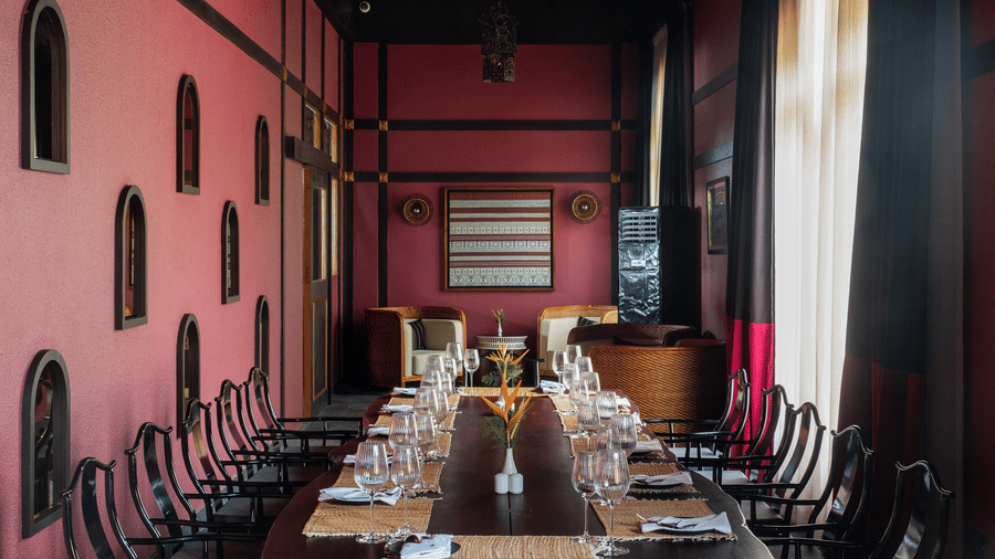 A wide interior shot of a long banquet table set for a large group inside the red-walled dining room at Rhino & River Wildlife Retreat & Spa, Pobitora.