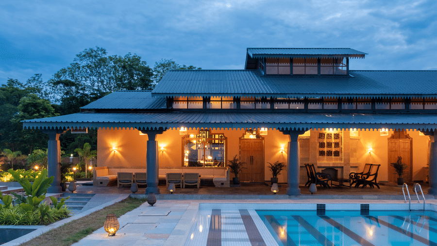 The main lodge of Rhino & River Wildlife Retreat & Spa, Pobitora, captured in the evening with warm lights reflecting in the swimming pool and highlighting the stone architecture.