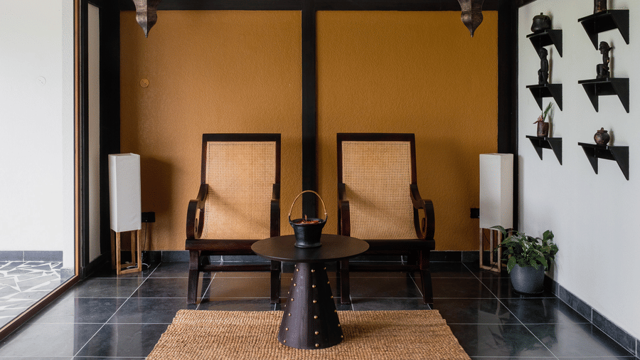 A waiting lounge with two high-backed wooden chairs and a yellow accent wall at Rhino & River Wildlife Retreat & Spa, Pobitora