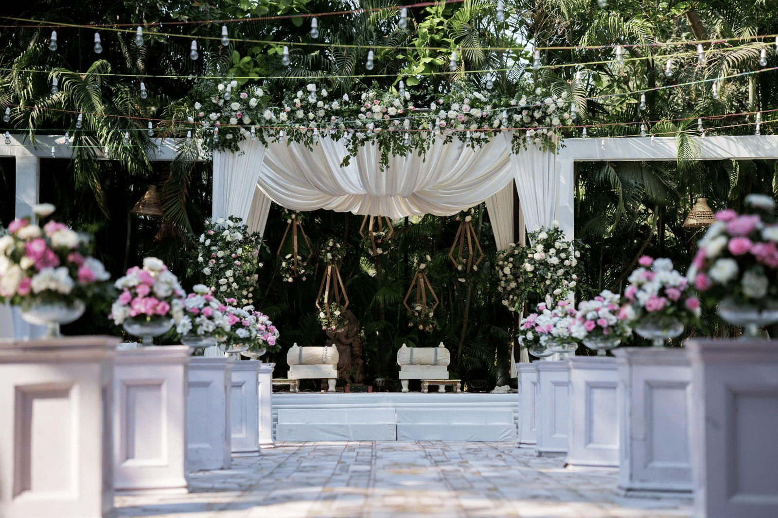 Outdoor wedding or event setup with a white canopy, floral arrangements of pink and white roses, and white pedestals.