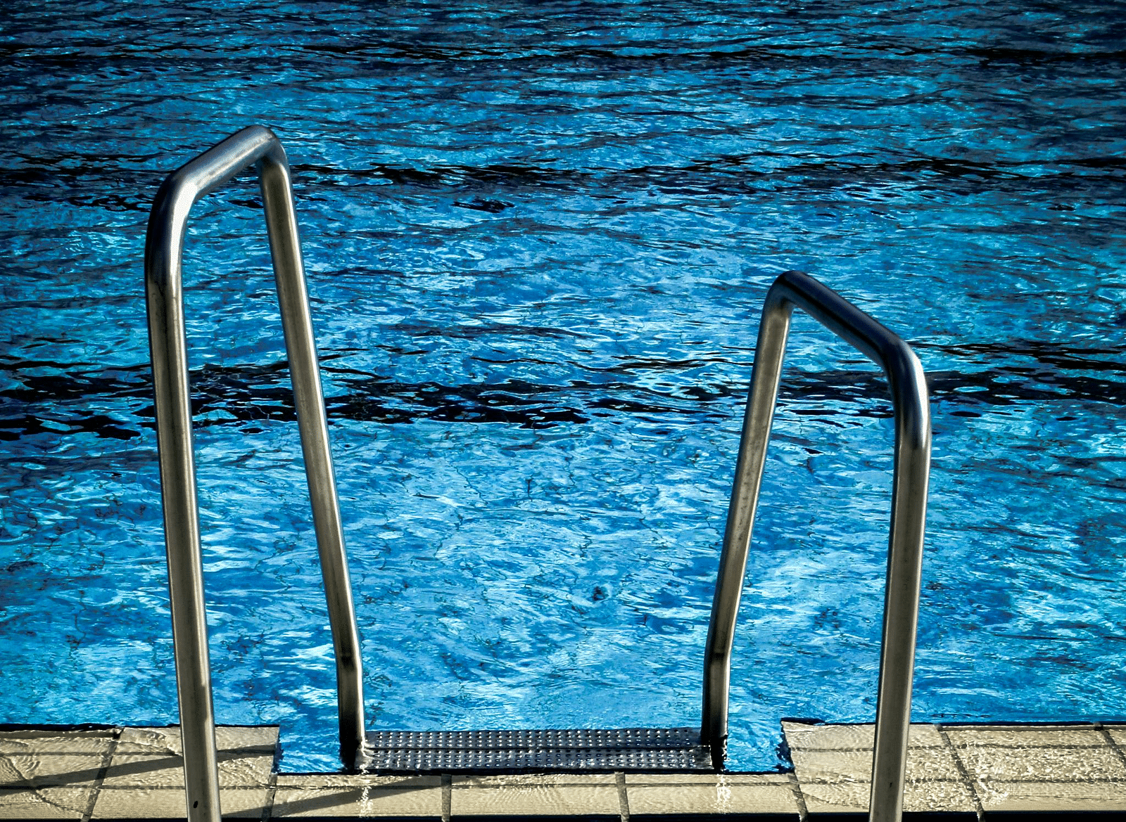 Two metal handrails lead into a swimming pool with blue water.