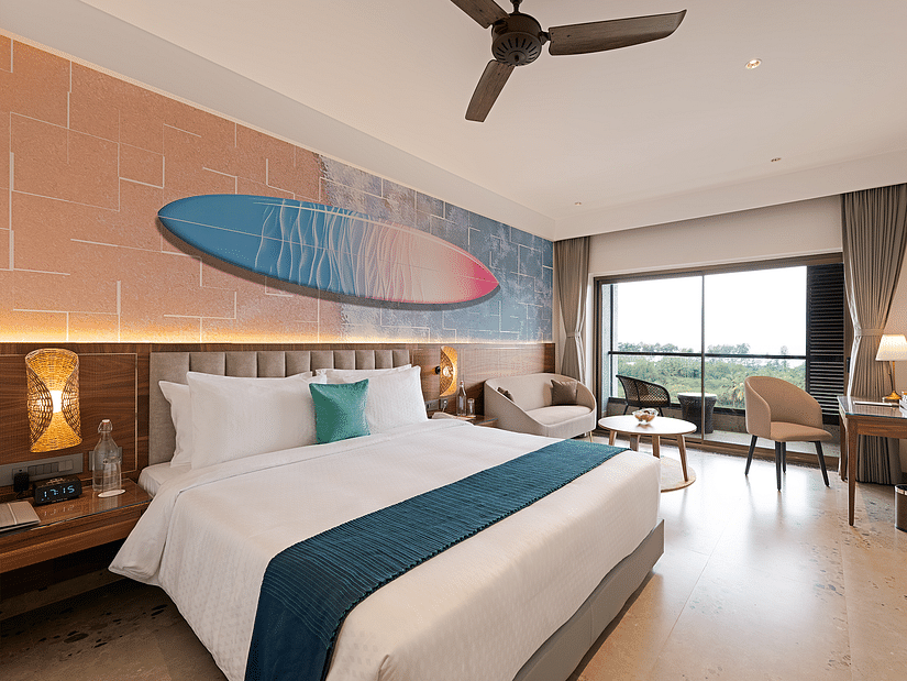 A double bed in one of the rooms at Cloud9 Sarovar Premiere, Palolem Goa, with a surfing board painting, adding coastal charm. One of the best hotels in South Goa for family stays