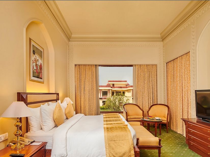 Luxury Suite featuring a king size bed, elegant gold accents, cosy seating area, large window, and views of landscaped gardens at The Ummed Jodhpur, Palace Resort and Spa