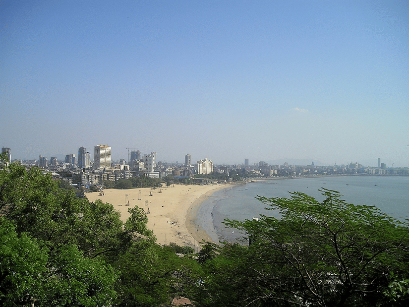 An aerial view of Mumbai's sky line in the distance with the Arabian Sea and a beach in view.