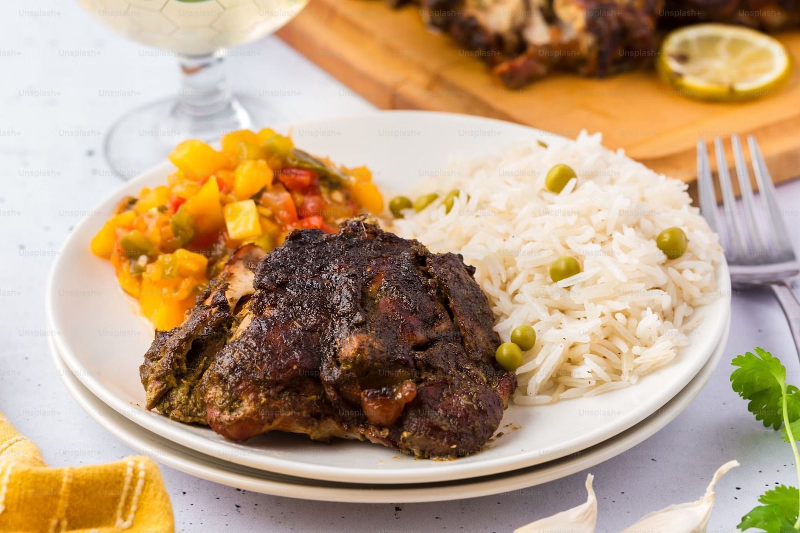 A plate holds a portion of cooked meat, rice with peas, and a side of stewed vegetables, presented as a meal.