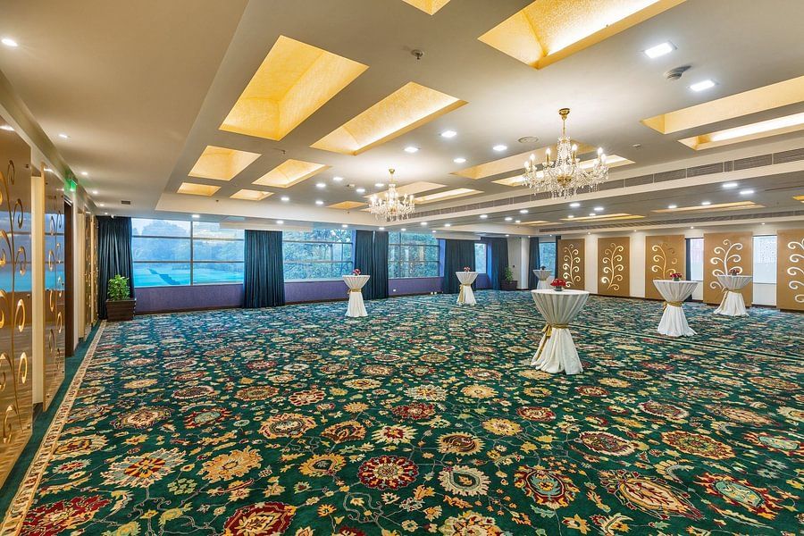 Spacious event hall with a patterned green carpet, elegant chandeliers, and draped cocktail tables - Heritage Village Resorts & Spa.