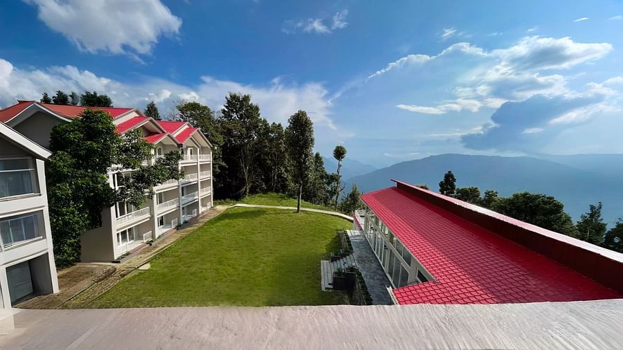 A scenic view of the buildings and landscape at Yashshree Resorts & Spa, Kalimpong, showcasing a distinctive red-roofed structure amidst the greenery and rolling hills.