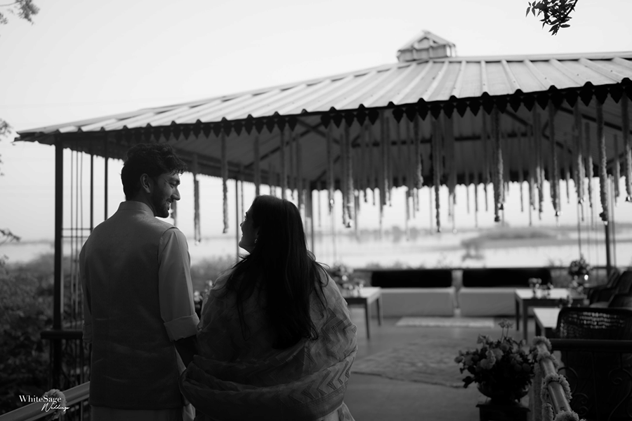 Black and white portrait of a couple standing inside an open-air lakeside pavilion structure at Umaid Palace.