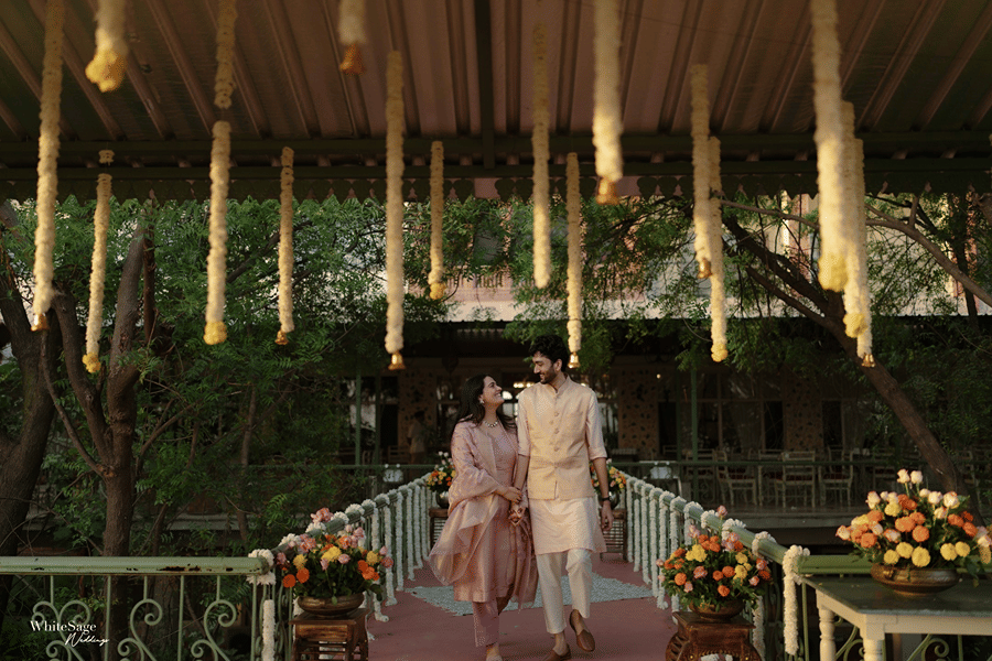 Couple strolling down a decorated bridge adorned with hanging flowers and marigold stands at Umaid Palace.