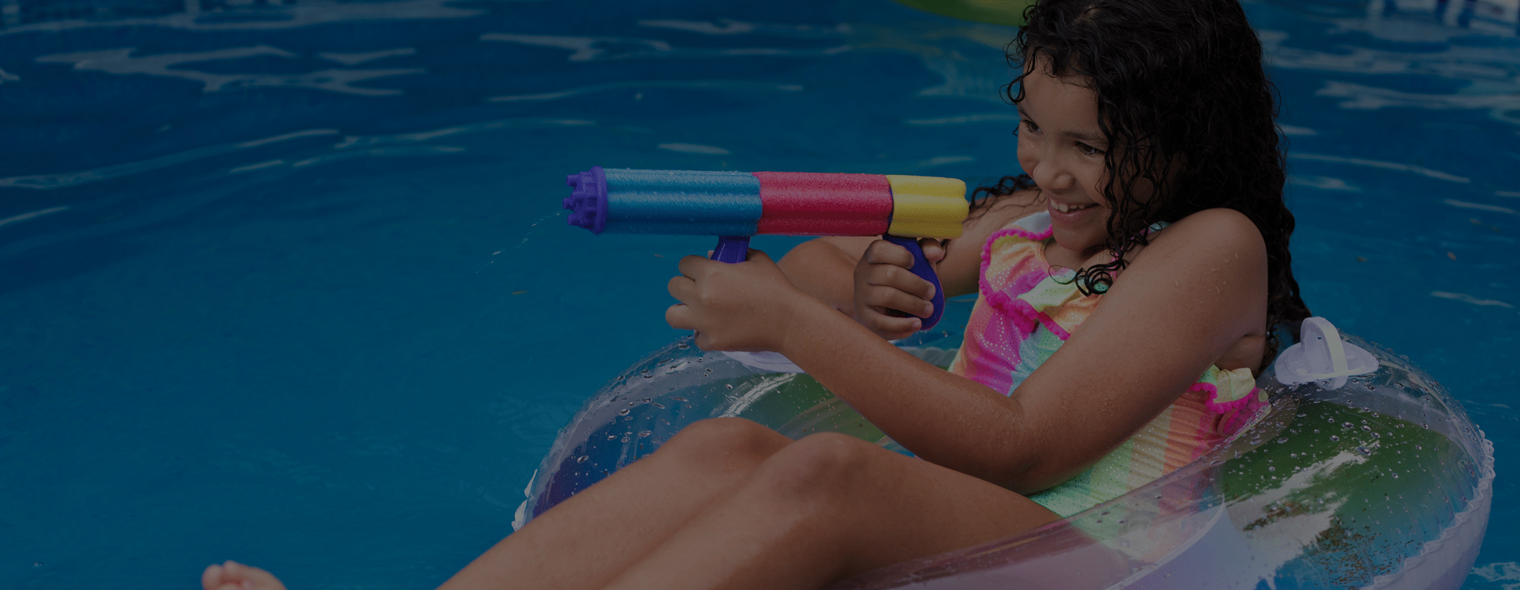 Person relaxing on a float in a swimming pool, holding a colorful water gun.