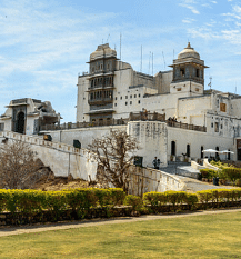 Palace with domes, viewed from a lawn, trees, sky with clouds.