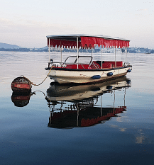 A small boat with a canopy floats on calm water, reflecting perfectly. 