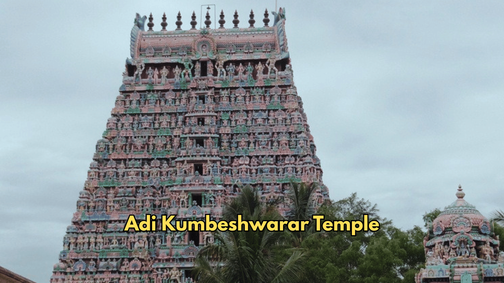 The tower of Adi Kumbeshwarar Temple rises against the sky. Shrines and foliage sit near the base of the structure.