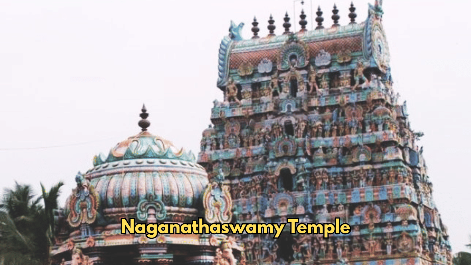 A dome sits next to the tower of Naganathaswamy Temple. Sculptures decorate the storeys of the tower.