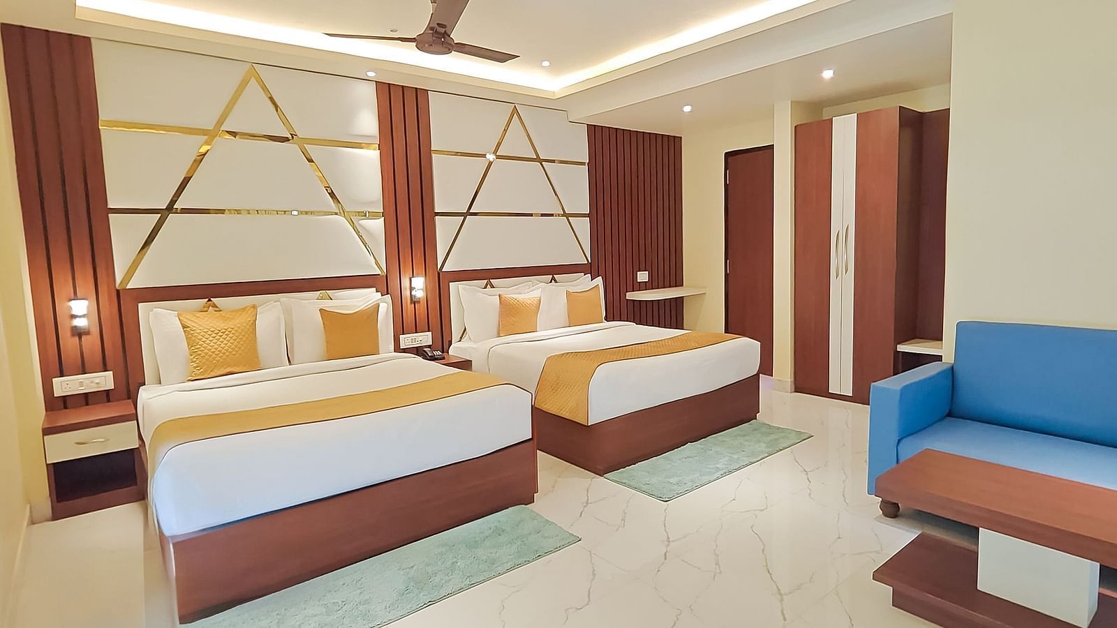 Family Room featuring two beds with wooden headboards, a blue armchair, and light-coloured walls at Yashshree Bangla Queen, Digha.