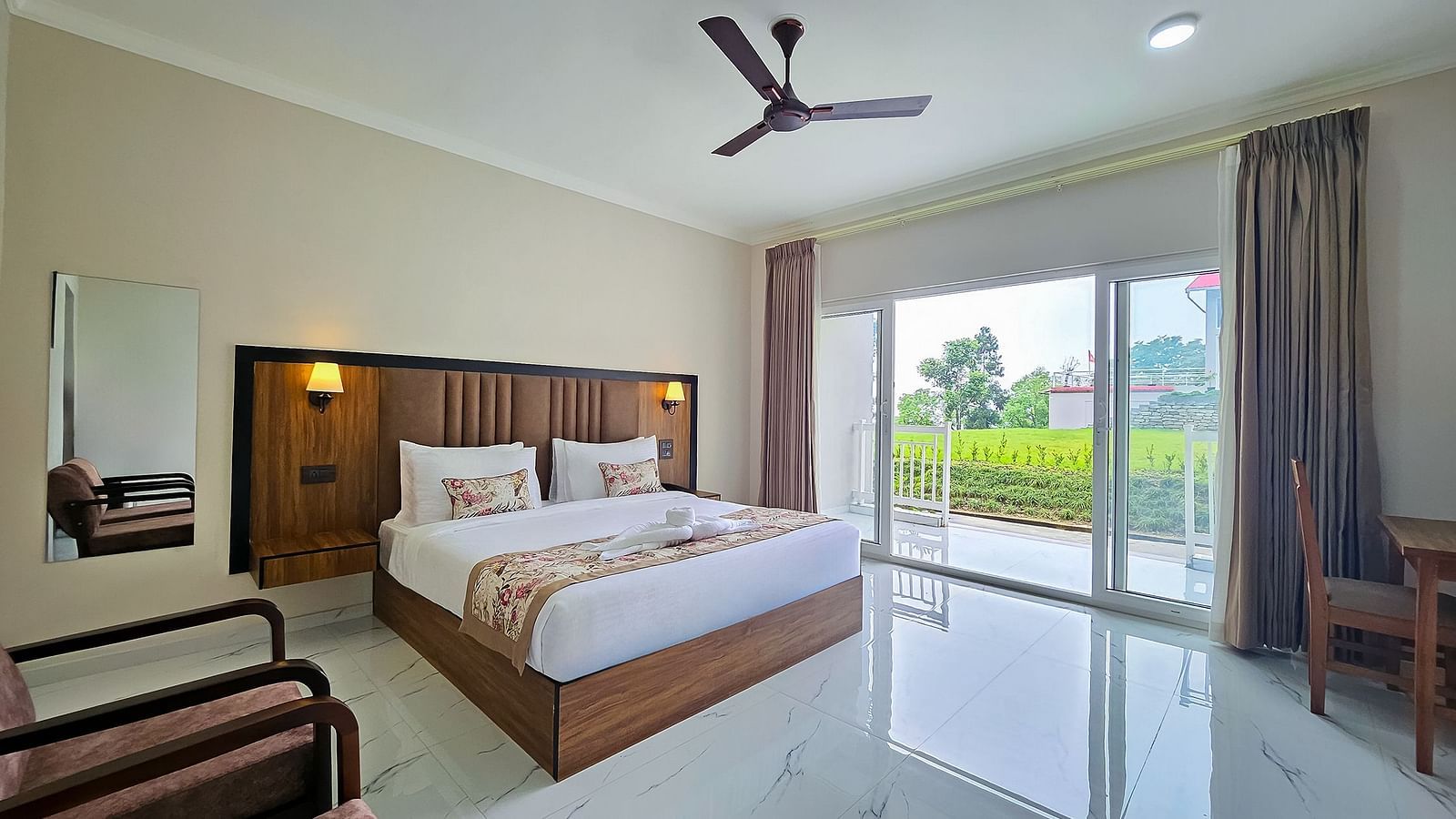  A spacious and bright hotel room at Yashshree Resorts & Spa, Kalimpong, featuring a comfortable bed, a ceiling fan, and large glass doors opening to a balcony.