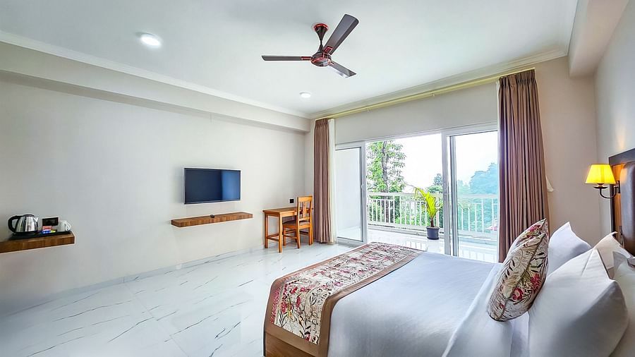 A bright and elegant bedroom with a large bed, flat-screen TV, and an open balcony, at Yashshree Resorts & Spa, Kalimpong.