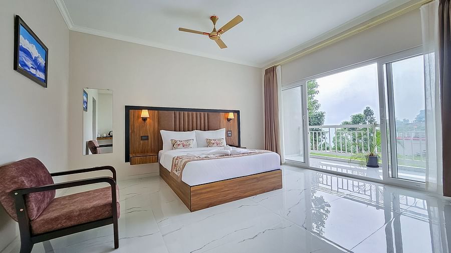 A cosy hotel room at Yashshree Resorts & Spa, Kalimpong, with a comfortable bed, a wooden headboard, and large windows offering natural light.