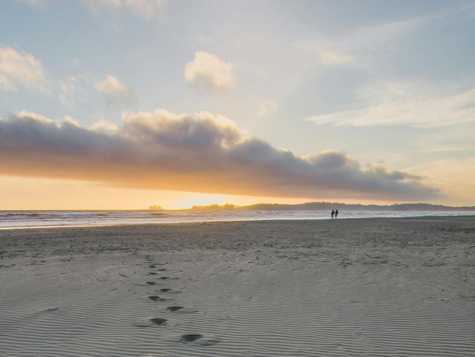 Footprints on the sand featuring the clouded sky and the hues of sunset.