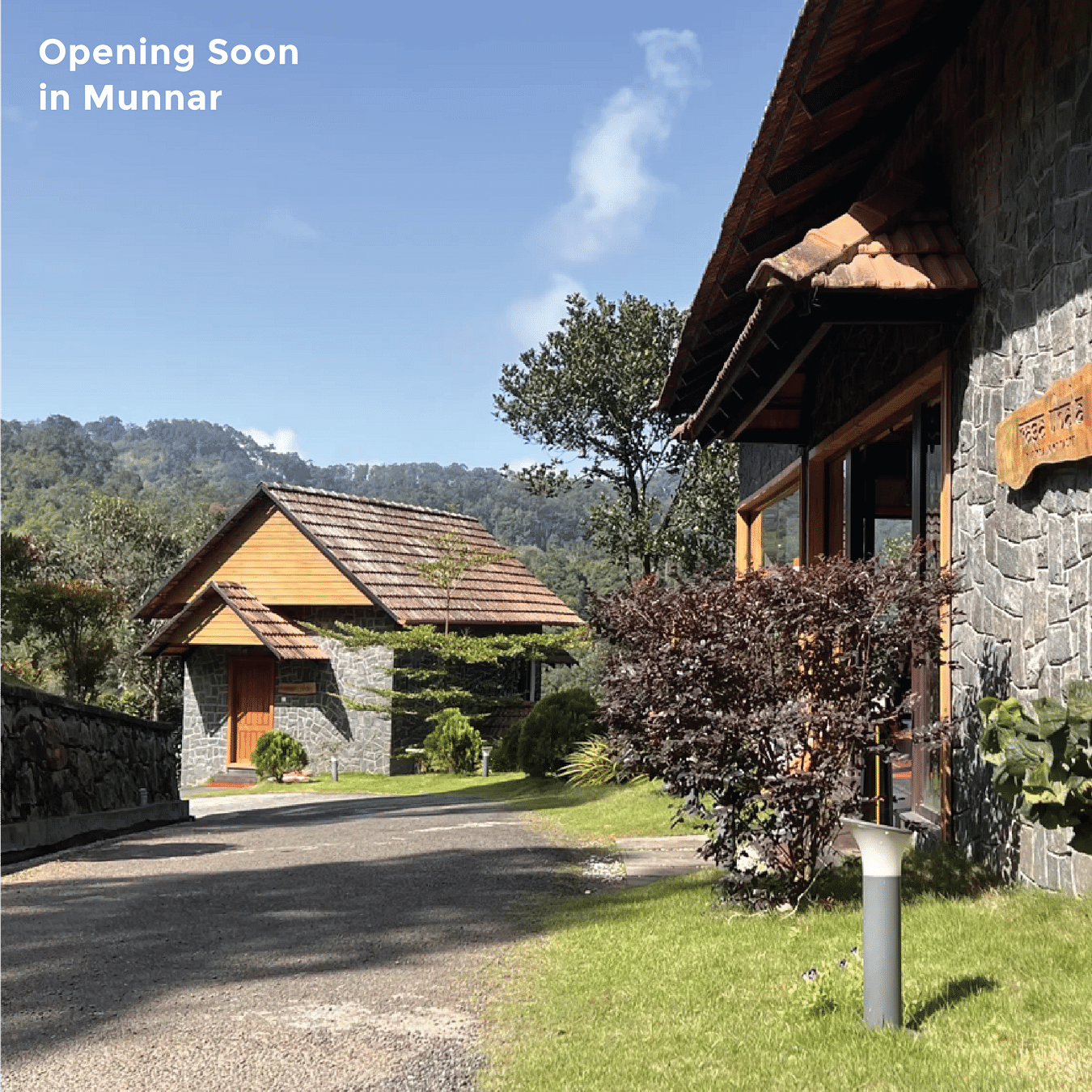 Two rustic stone and wood buildings with tiled roofs are nestled in a lush green landscape under a bright sky with text - Opening Soon in Munnar.