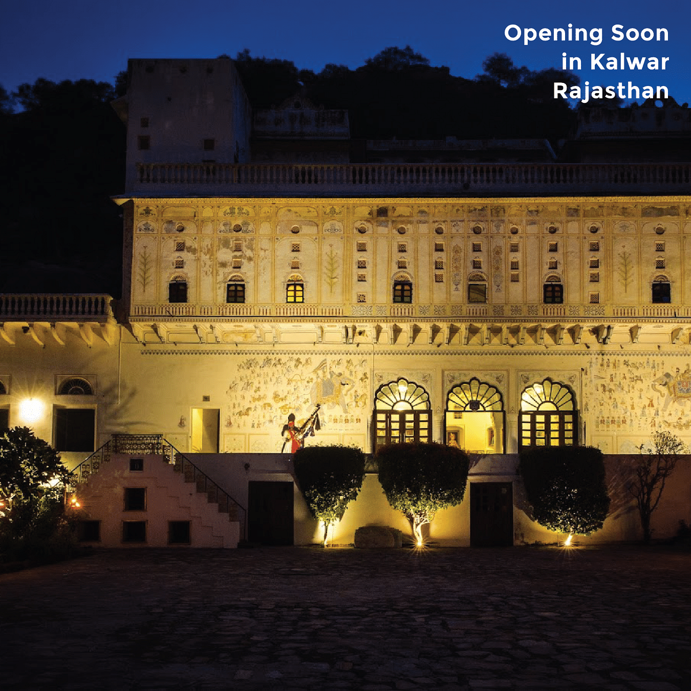 An illuminated fort is captured at night, showcasing its traditional architecture and artwork with text - Opening Soon in Kalwar Rajasthan.